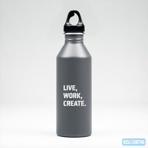 May include: A grey stainless steel water bottle with a black lid and a carrying handle. The bottle has the text "LIVE, WORK, CREATE." printed in white on the front.
