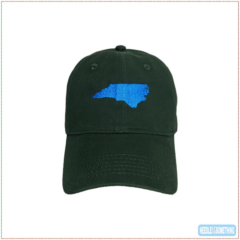 May include: A dark green baseball cap with a blue embroidered outline of the state of North Carolina. The cap has a curved brim and an adjustable strap. The text "NEEDLE & SOMETHING" is in the bottom right corner.