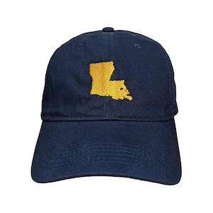 May include: A navy blue baseball cap featuring an embroidered gold-colored map of the state of Louisiana centered on the front panel. The cap has a curved brim with visible stitching and a button at the top center of the crown.