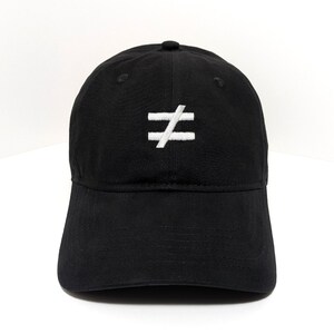 Puede incluir: Una gorra de béisbol negra con un símbolo de desigualdad bordado en blanco centrado en el panel frontal. La gorra tiene una corona estructurada, una visera curva y un botón en la parte superior, confeccionada en tela negra con costuras a juego.