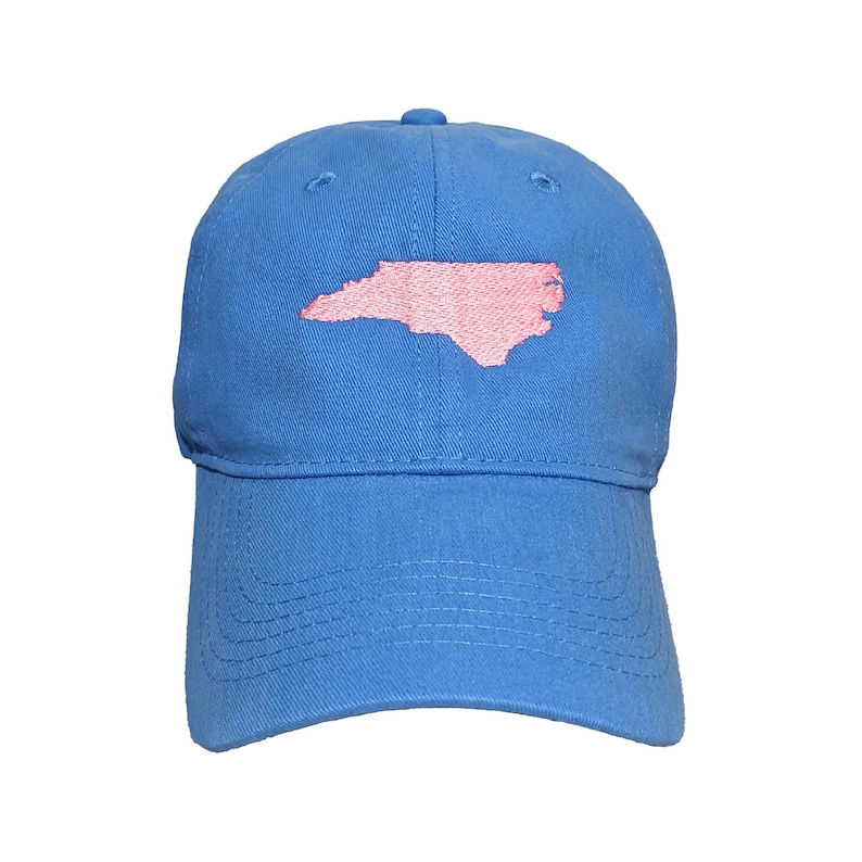 May include: A blue baseball cap with a pink embroidered outline of the state of North Carolina. The cap has a curved brim and an adjustable strap at the back. The hat is made of a soft, durable fabric.