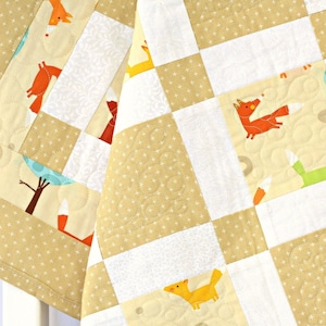 May include: A beige and white patchwork quilt with a repeating pattern of foxes and other woodland creatures. The quilt is made of different fabrics with a variety of textures.