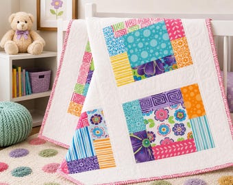 May include: A patchwork baby quilt featuring a white background with blocks of colorful fabric patterns including floral, polka dot, striped, and geometric designs in shades of pink, purple, blue, orange, yellow, and green with pink trim.