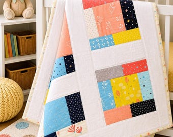 May include: A patchwork baby quilt featuring a white background with rectangular blocks in coral, navy blue, yellow, and light blue. The fabric patterns include floral prints, small crosses, and solid colors, finished with a light yellow patterned border.