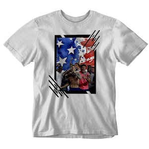 May include: White t-shirt with a black and white graphic of a group of soccer players celebrating in front of an American flag.