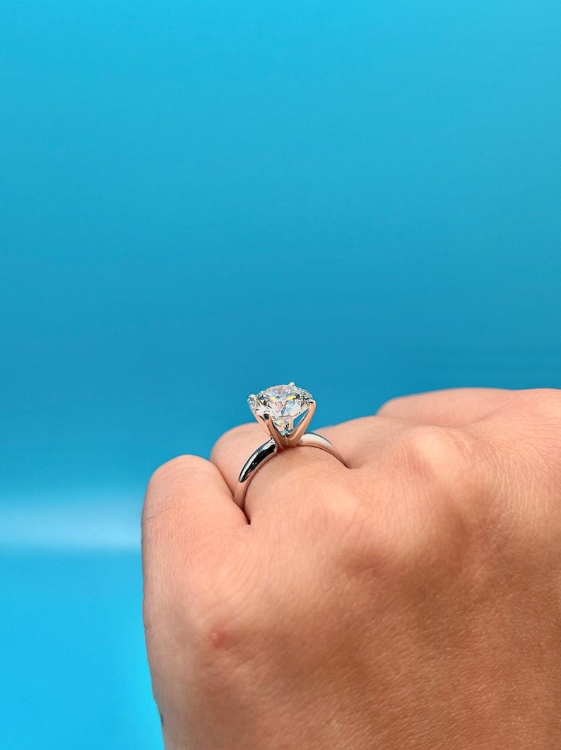 May include: A silver engagement ring with a large, round, clear diamond set in a prong setting.