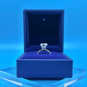 May include: A silver ring with a large, clear diamond in a blue velvet ring box.