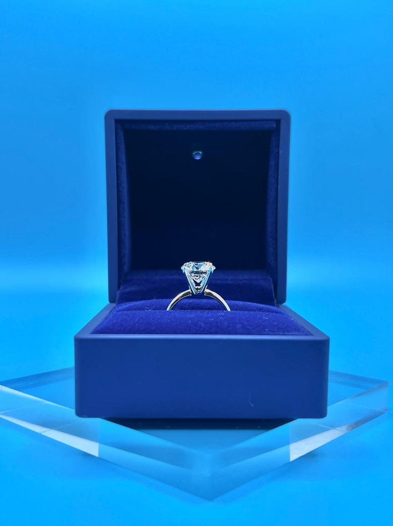 May include: A silver ring with a large, clear diamond in a blue velvet ring box.