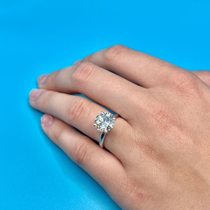 May include: A silver ring with a large, round, clear diamond set in a prong setting.