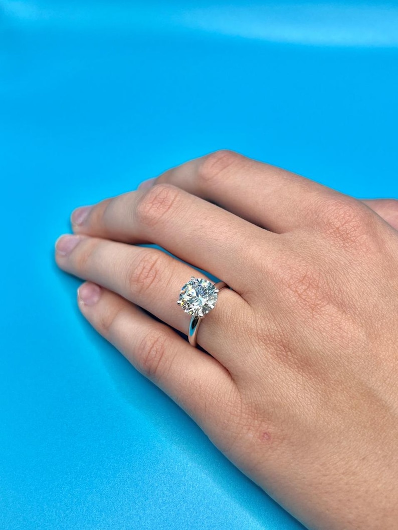 May include: A silver ring with a large, round, clear diamond set in a prong setting.
