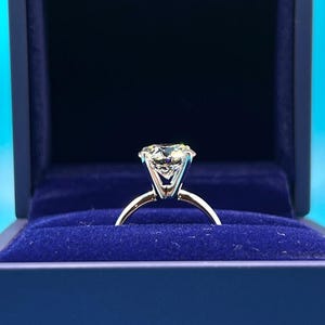 Close-up of a 4 carat round lab grown diamond engagement ring set in 14K gold solitaire setting, shown on a neutral background.