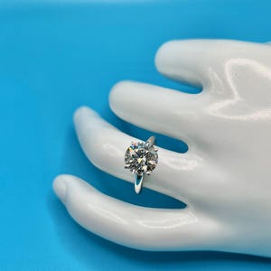 May include: A silver solitaire engagement ring with a large, round, clear diamond set in a simple band.
