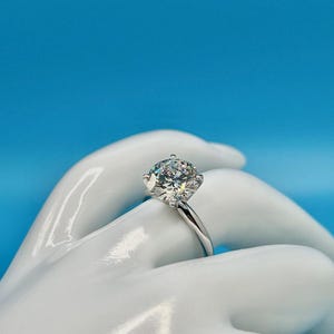 May include: A silver solitaire engagement ring with a large, round, clear diamond.