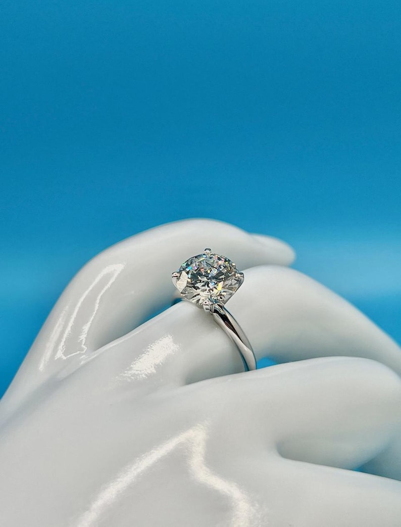 May include: A silver solitaire engagement ring with a large, round, clear diamond.