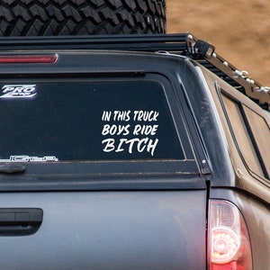 Pode incluir: Uma caminhonete cinza com uma grade de tejadilho preta e um pneu sobressalente. A janela traseira tem um decalque branco com o texto "IN THIS TRUCK BOYS RIDE BITCH". A imagem também inclui o texto "Inspire2CreateShop Decal".