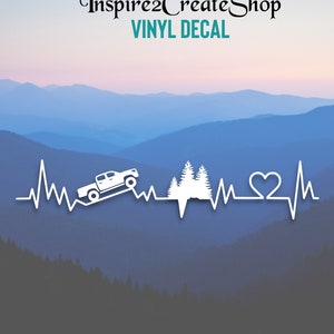 Pode incluir: Adesivo de vinil branco com um design de batimento cardíaco com um caminhão, árvores e um coração. O texto "Inspire2CreateShop" e "VINYL DECAL" estão no topo. O fundo mostra uma cordilheira.