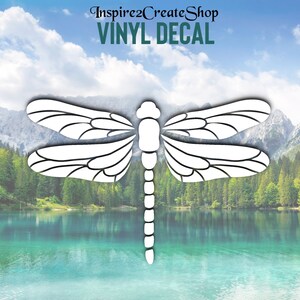 Pode incluir: Vinil branco com decalque de libélula com padrões de asas detalhados. A libélula está centrada em um fundo de lago, montanhas e céu. O texto "Inspire2CreateShop VINYL DECAL" está no topo.