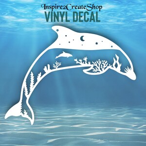 Pode incluir: Vinil branco em forma de golfinho, com uma cena subaquática no interior. A cena inclui um golfinho, corais e um céu noturno com estrelas e uma lua crescente. O texto "VINYL DECAL" está no topo.
