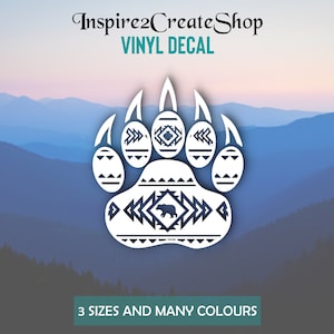 Peut inclure: Autocollant en vinyle blanc représentant une patte d'ours avec des motifs géométriques. Le texte "Inspire2CreateShop VINYL DECAL" est en haut. Le texte "3 TAILLES ET BEAUCOUP DE COULEURS" est en bas. Le fond est un paysage de montagne.
