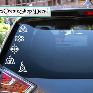 Pode incluir: Autocolantes de vinil branco com desenhos de nós celtas são exibidos no vidro traseiro de um carro. Os autocolantes incluem vários padrões de nós, como o nó da Trindade e o nó do amor celta. O texto "Inspire2CreateShop Decal" é visível.