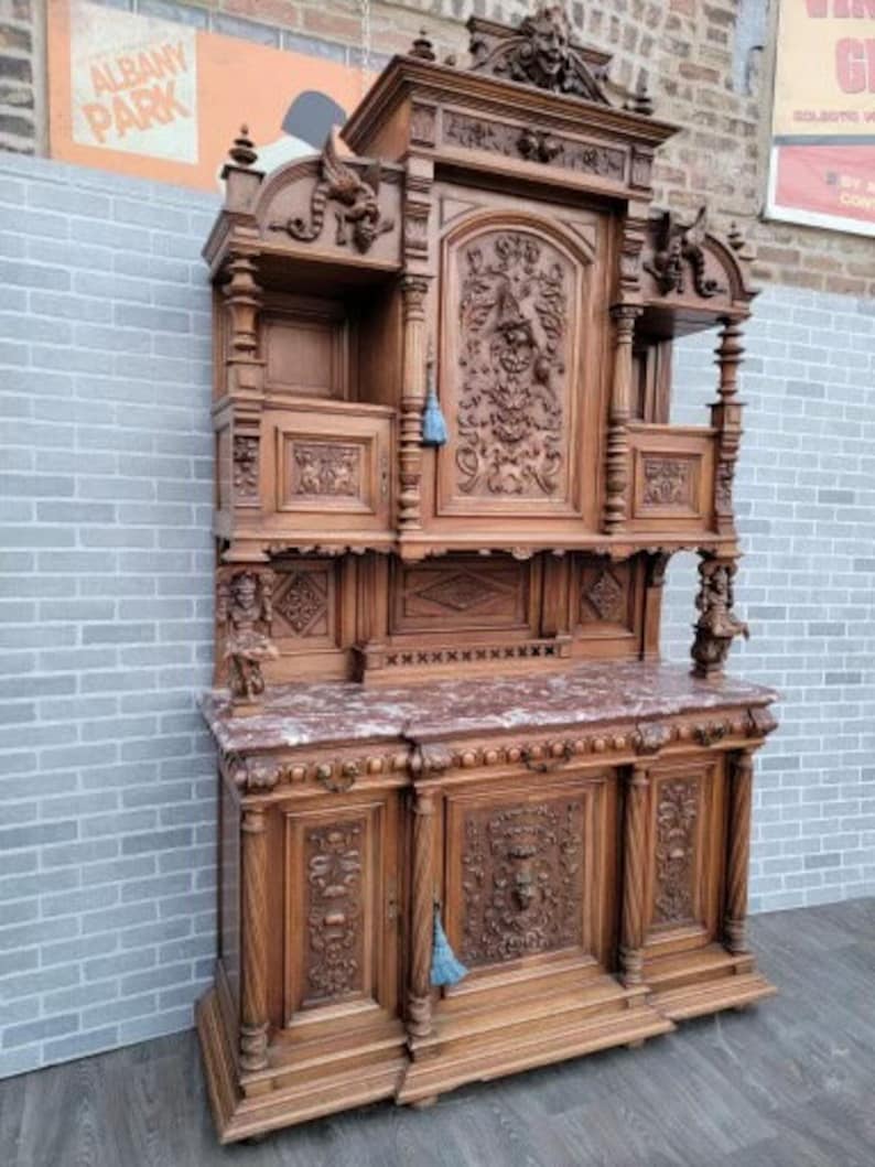 May include: A large, intricately carved wooden cabinet with a marble top. The cabinet has two doors on the bottom and a glass-fronted cabinet on top. The cabinet is decorated with ornate carvings of flowers, leaves, and other designs.