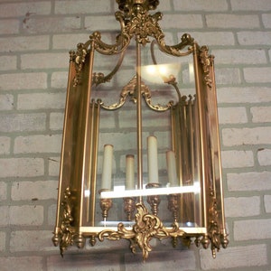 Puede incluir: Una lámpara de araña de vidrio adornada con un diseño decorativo en espiral. La lámpara de araña es de color dorado y tiene seis bombillas de estilo candelabro.