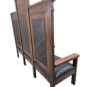 May include: A tall wooden bench featuring a high backrest with three distinct sections. Each section contains a dark, smooth, leather-like panel secured with metal studs. The bench has straight wooden armrests and a matching dark seat cushion.