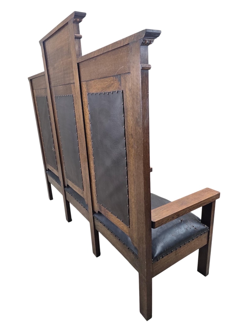 May include: A tall wooden bench featuring a high backrest with three distinct sections. Each section contains a dark, smooth, leather-like panel secured with metal studs. The bench has straight wooden armrests and a matching dark seat cushion.