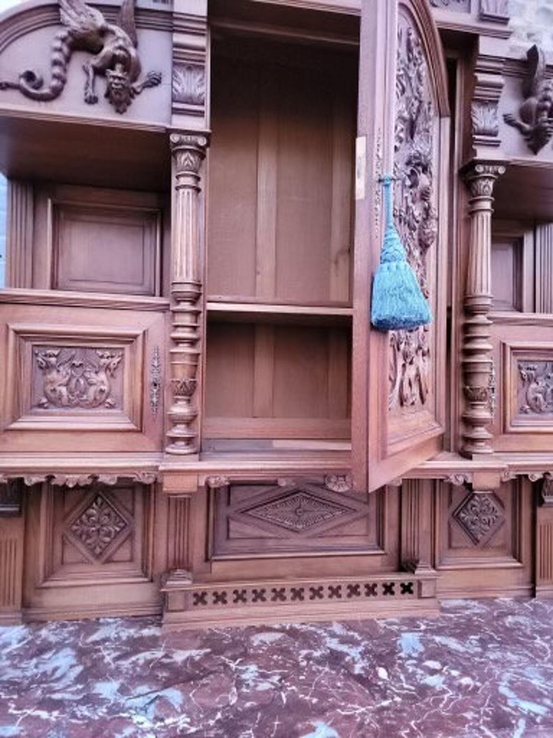 May include: A large, intricately carved wooden cabinet with multiple shelves and doors. The cabinet features ornate details, including a dragon sculpture on the top and a blue tassel hanging from one of the doors.