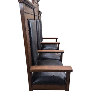 May include: A tall wooden bench with a dark brown finish and black leather upholstery. The piece features high, straight backrests with decorative molding at the top, flat armrests, and a series of seats lined up in a row with metal nailhead trim.