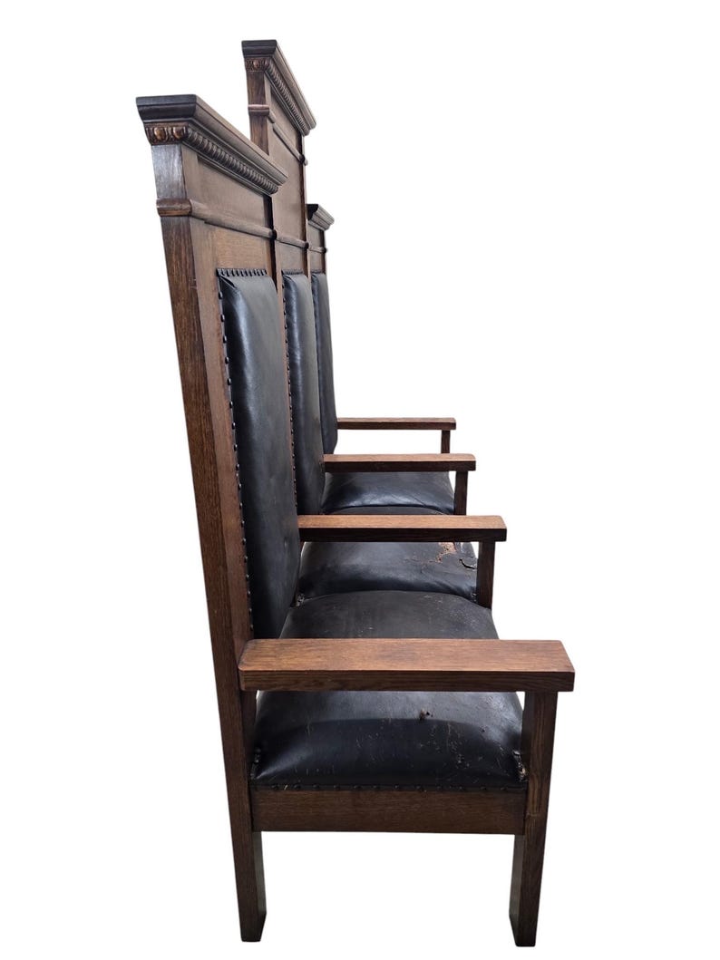 May include: A tall wooden bench with a dark brown finish and black leather upholstery. The piece features high, straight backrests with decorative molding at the top, flat armrests, and a series of seats lined up in a row with metal nailhead trim.