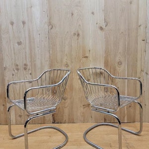 May include: Two chrome wire chairs with a curved back and a curved seat. The chairs are on a wooden floor.