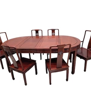 May include: A dark reddish-brown wooden dining set consisting of an oval table and six matching chairs. Each chair features a high backrest with a circular decorative inlay. The table has a smooth, polished surface with visible wood grain.