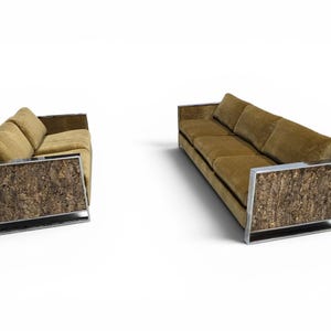 May include: A set of two sofas upholstered in olive green velvet fabric. Each sofa features a rectangular frame made of polished chrome metal with side panels covered in a textured, natural brown tree bark material.