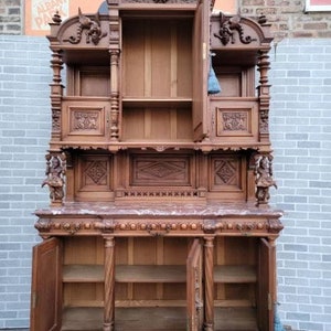 May include: A large, antique, wooden cabinet with intricate carvings. The cabinet has two doors on the bottom and two shelves on the top. The cabinet is made of dark wood and has a marble top.