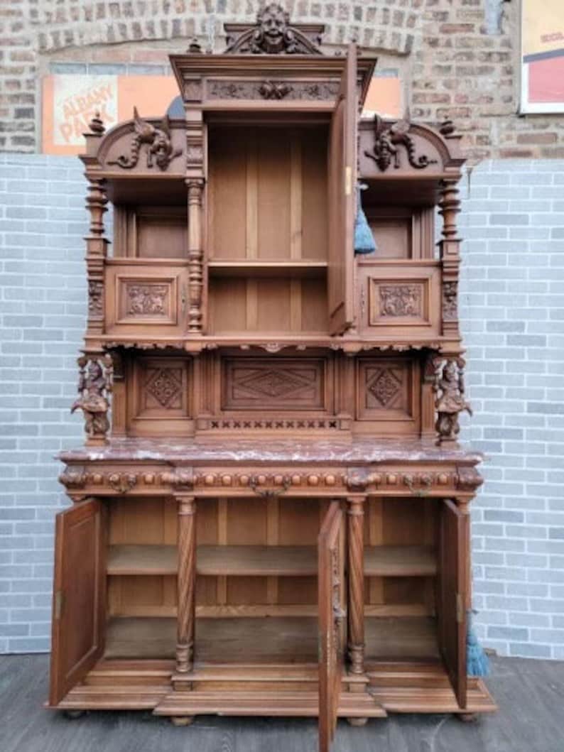 May include: A large, antique, wooden cabinet with intricate carvings. The cabinet has two doors on the bottom and two shelves on the top. The cabinet is made of dark wood and has a marble top.