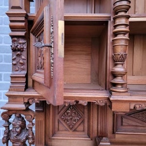 May include: A large, intricately carved wooden cabinet with a glass door and multiple shelves. The cabinet is made of dark wood and has a rich, antique finish.