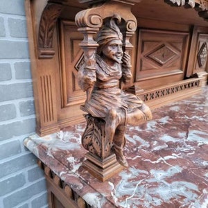 May include: A wooden cabinet with intricate carvings and a marble top. The cabinet features a carved figure of a man with a beard and a hat. The cabinet is a beautiful example of antique furniture.