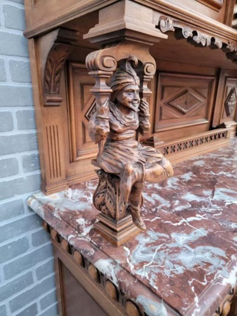 May include: A wooden cabinet with intricate carvings and a marble top. The cabinet features a carved figure of a man with a beard and a hat. The cabinet is a beautiful example of antique furniture.