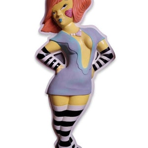 May include: A figurine of a woman with red hair, wearing a light blue dress with a plunging neckline, black and white striped stockings, and black and white striped gloves. She has yellow skin and a pink heart on each cheek.