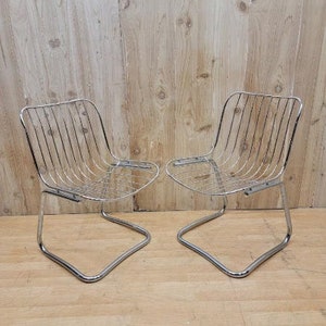 May include: Two chrome wire chairs with a simple, modern design. The chairs have a curved, open frame and a wire seat and back.