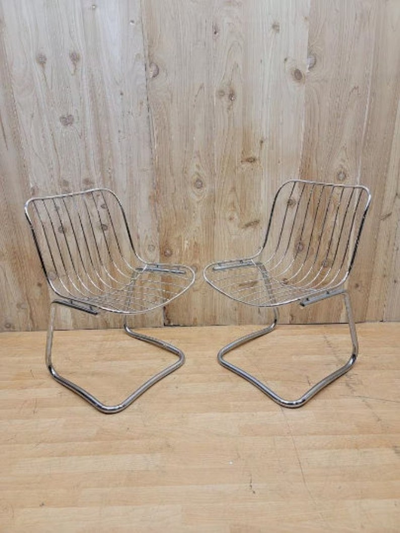 May include: Two chrome wire chairs with a simple, modern design. The chairs have a curved, open frame and a wire seat and back.