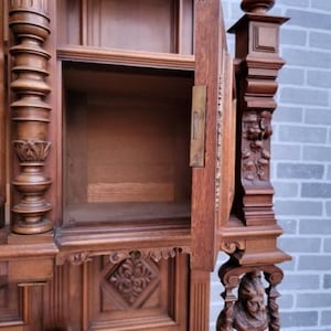 May include: A large, intricately carved wooden cabinet with a glass door and shelves. The cabinet has a dark brown finish and features ornate details, including a carved floral design and a decorative metal hinge.
