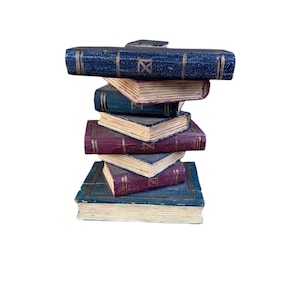 May include: A stack of six antique-style books with blue and burgundy covers. The books are arranged in a precarious tower, with the top book featuring a clasp. The edges of the pages are aged, giving them a vintage appearance.