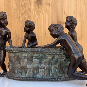 Puede incluir: Una escultura de bronce de cinco niños jugando alrededor de una cesta. Los niños están todos desnudos y tienen rasgos realistas. La escultura es un hermoso ejemplo de la habilidad del artista.
