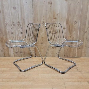 May include: Two chrome wire chairs with a curved back and a simple design. The chairs are on a wooden floor.