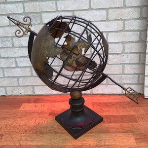 May include: A decorative metal globe with a black wooden base and a gold arrow pointing to the right. The globe is made of wire and has a gold-colored map on it.