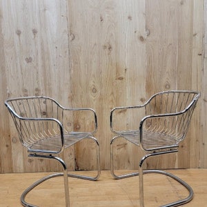 May include: Two chrome wire chairs with a curved back and a curved seat. The chairs are on a wood floor.