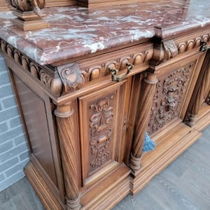 May include: A large, intricately carved wooden cabinet with a marble top. The cabinet has multiple doors and drawers, and features ornate details like floral carvings and decorative hardware.
