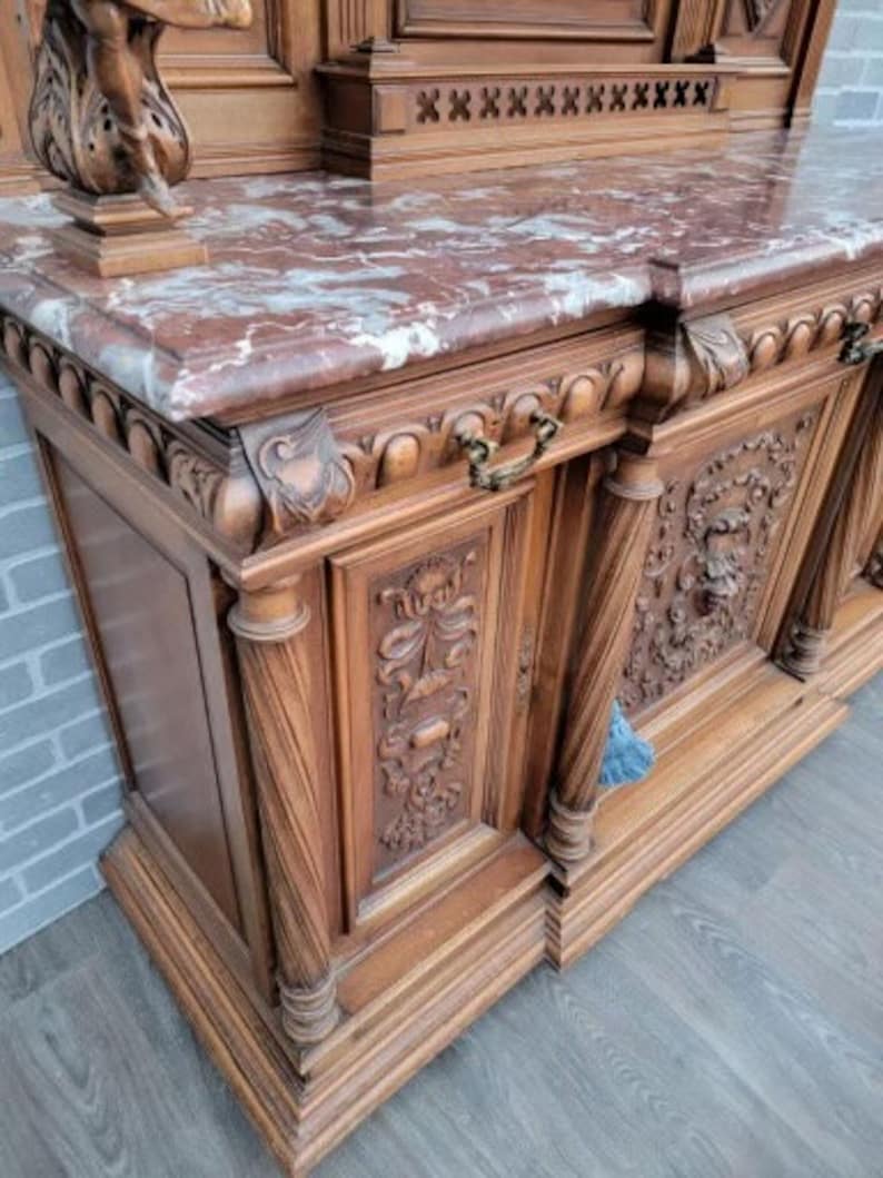May include: A large, intricately carved wooden cabinet with a marble top. The cabinet has multiple doors and drawers, and features ornate details like floral carvings and decorative hardware.